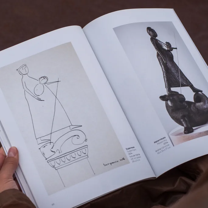 The catalogue held open on a spread: a sketch of a figure on a plinth facing the finished bronze